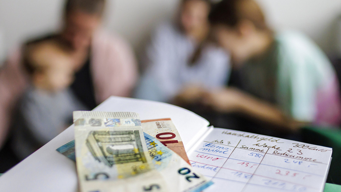 Eine Mutter sitzt mit ihren drei Kindern vor einem Haushaltsbuch mit fünfunddreißig Euro
